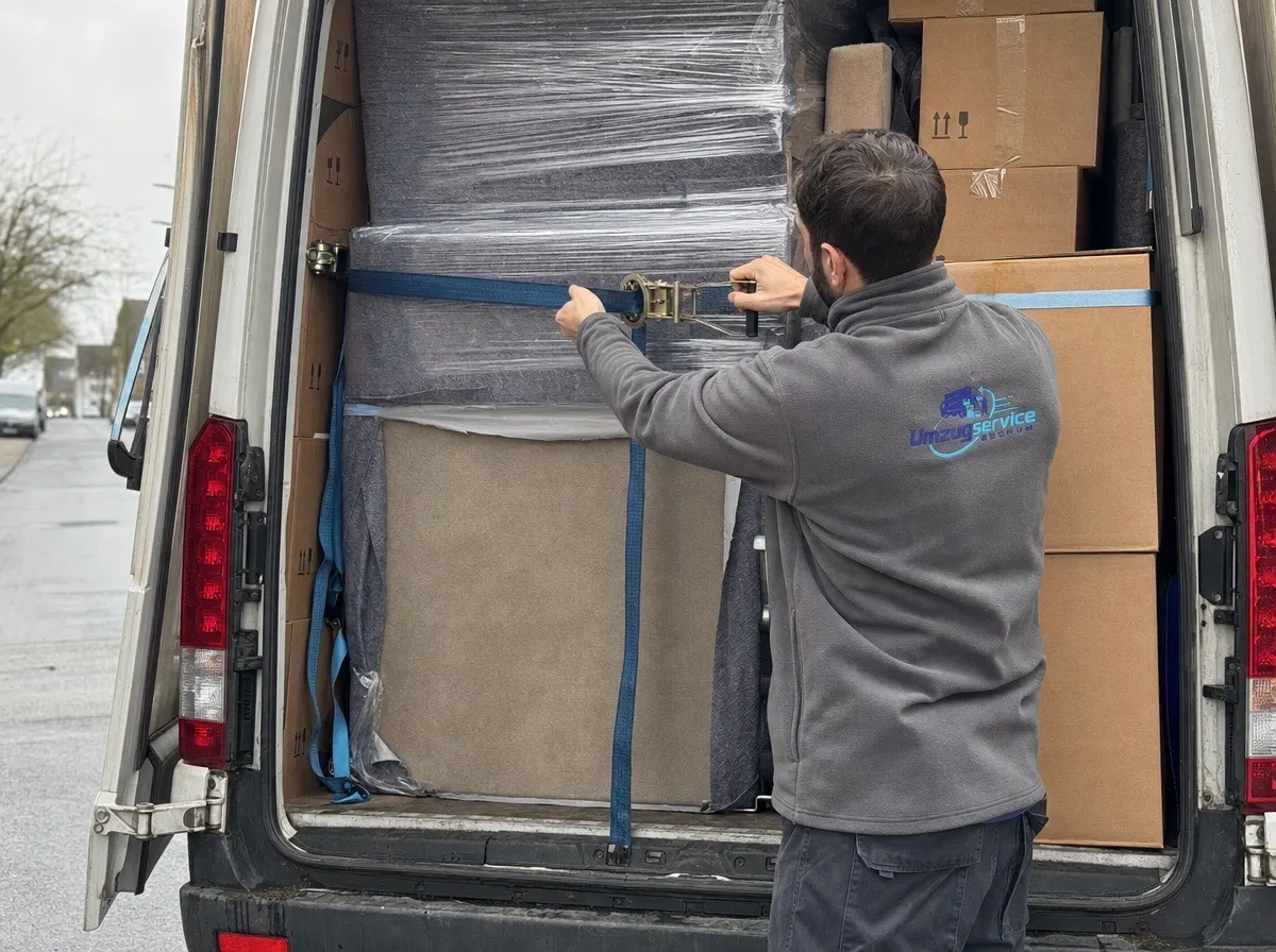 Ein Möbelpacker zurrt einen Spanngurt an der Ladung im beladenen Transporter fest.